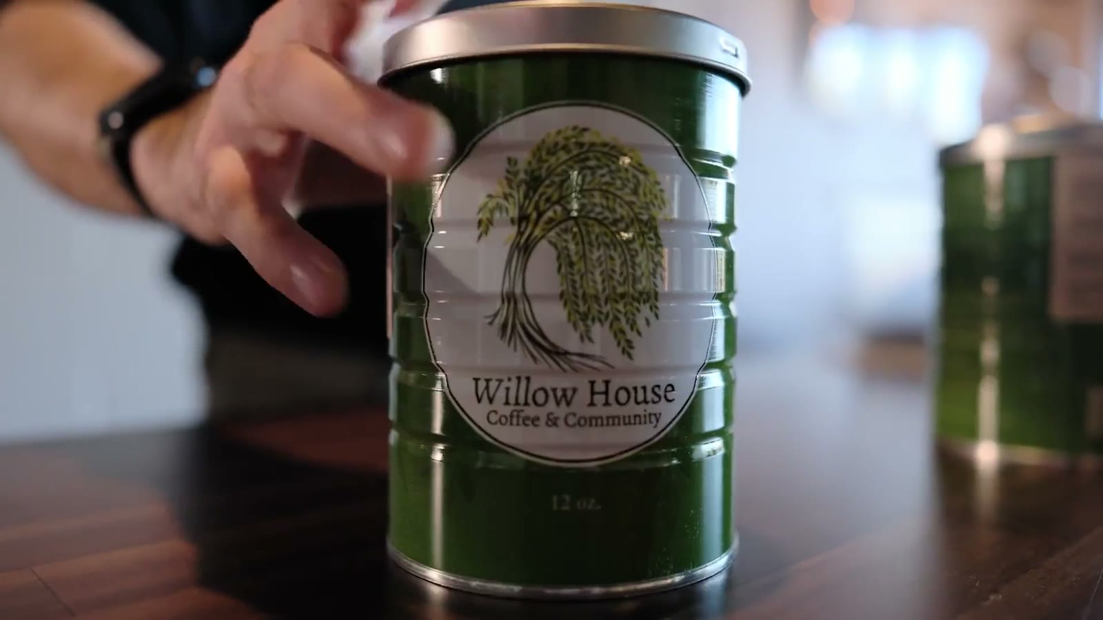 A hand reaching for a Willow House Coffee tin, the brand rendered as a physical product